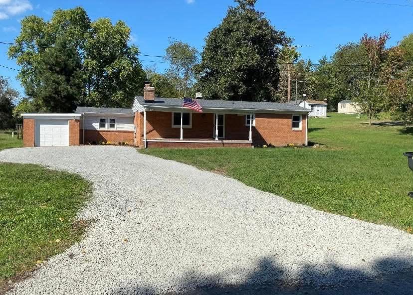 The same brick ranch after, with a cleared yard and gravel driveway