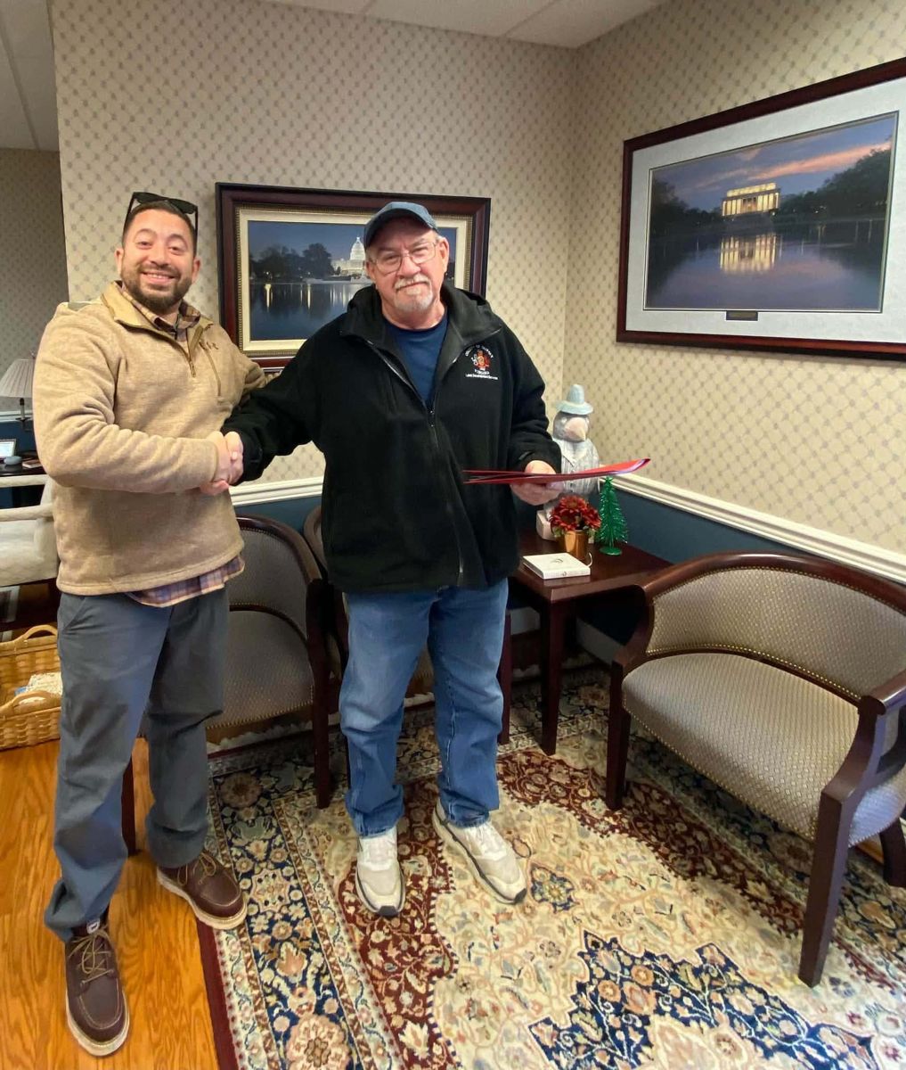 A Real Hope team member shaking hands with a homeowner holding a red folder