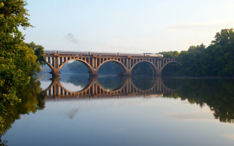 The railroad bridge over the Rappahannock River at Fredericksburg, reflected in still water at sunrise