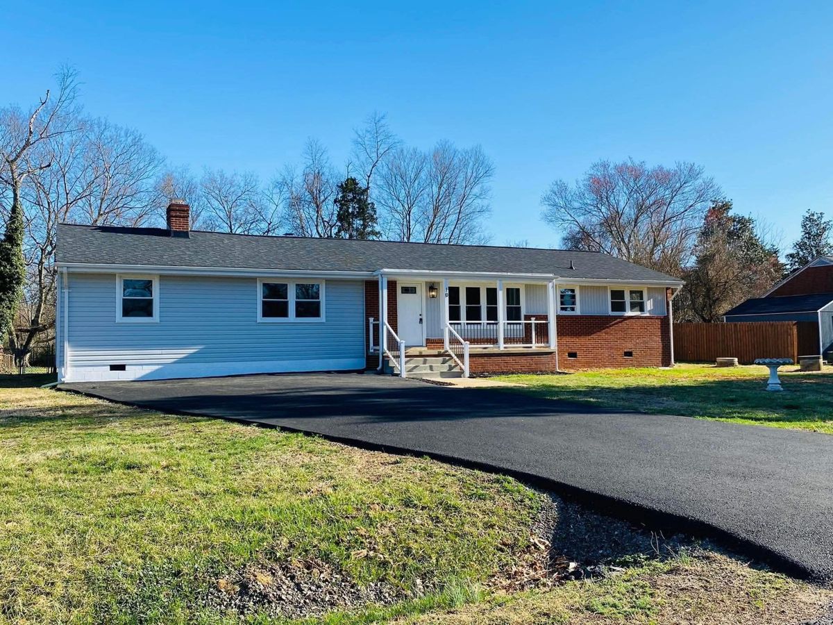The same ranch house after: new siding, roof, porch railings and a paved driveway