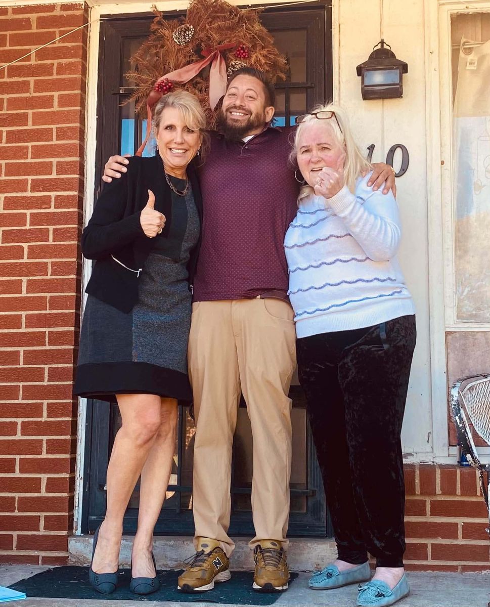 Two homeowners and a Real Hope team member giving a thumbs up on the front porch